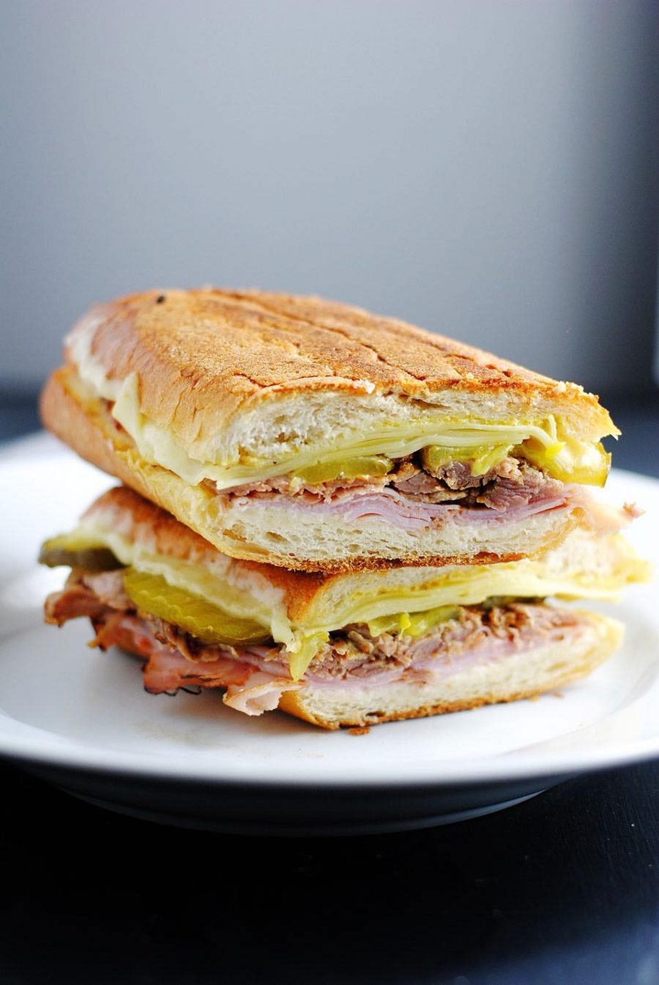 A Cuban sandwich, cut in half and stacked, revealing ham, roasted pork, Swiss cheese, and pickles.
